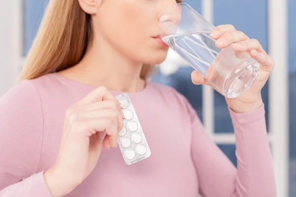 Young woman taking pills and drinking water
