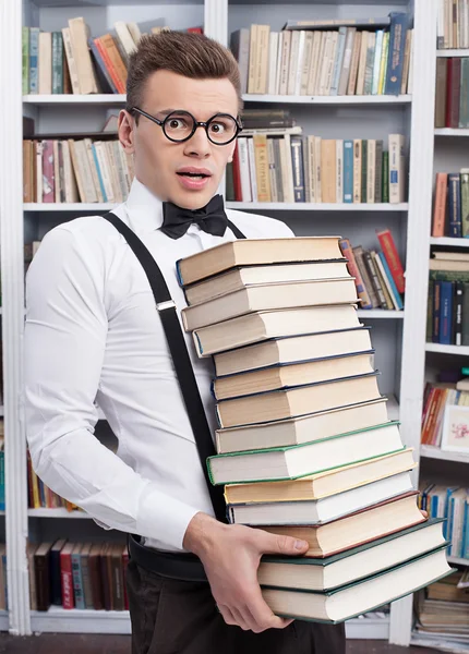 Shocked young man carrying a heavy book stack