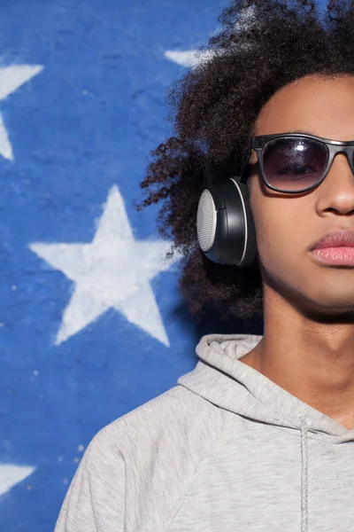 Music lover. Cropped image of confident young African man in headphones standing against American flag and listening to the music