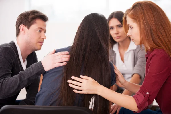 Rear view of depressed woman sitting while other people comforting her