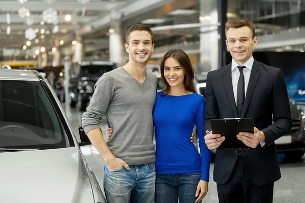 Couple and handsome car salesman standing at the dealership
