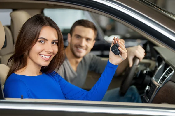 Couple sitting inside of their new car while woman showing keys