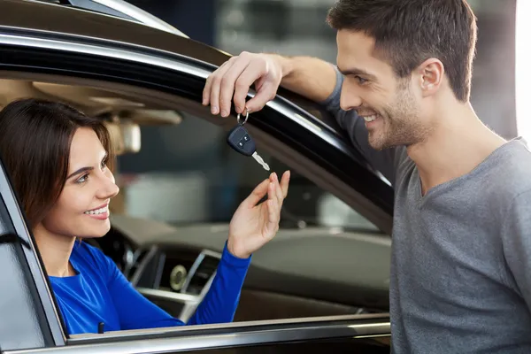 Men standing near the car at the dealership and giving a key to his girlfriend