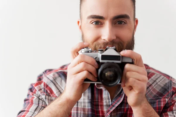 Young beard man focusing at you with his retro camera