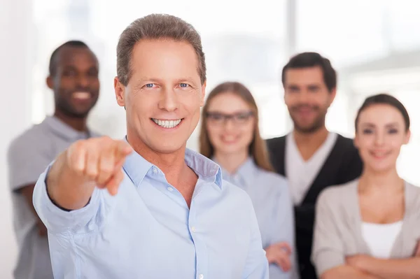 Man pointing you and smiling while group of people standing on background