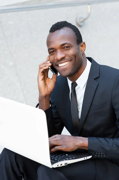 African man talking on phone and working on laptop