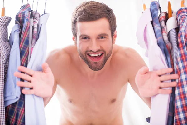 Shirtless man looking through a various shirts