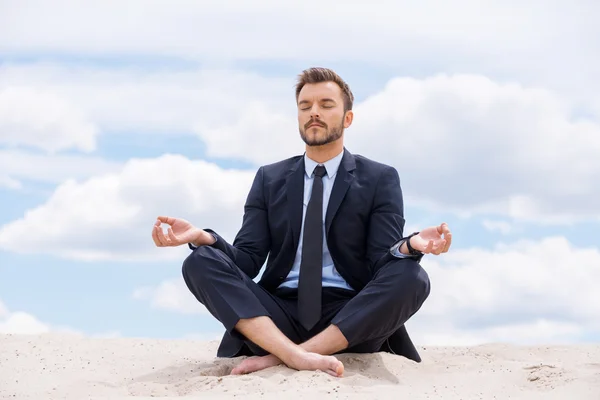 Businessman meditating on sand