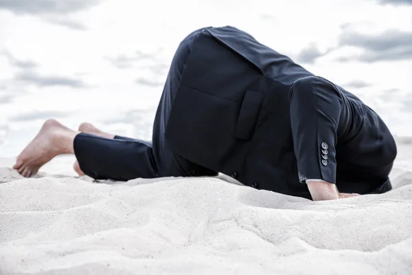 Man in formal wear hiding his head in sand