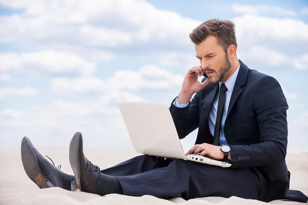 Man in formal wear working on laptop in desert