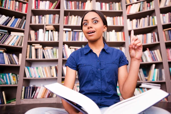 African female student holding a book and pointing up