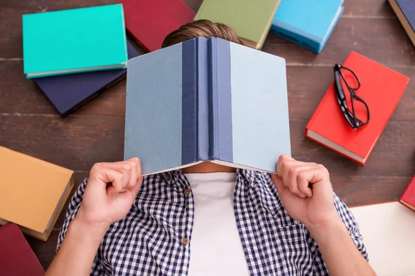 Young man covering his face with books