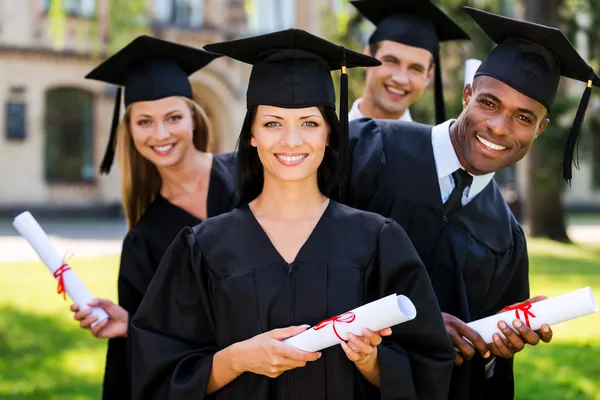 Four college graduates holding diplomas