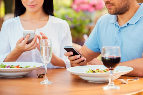 Couple typing on smart phones in restaurant