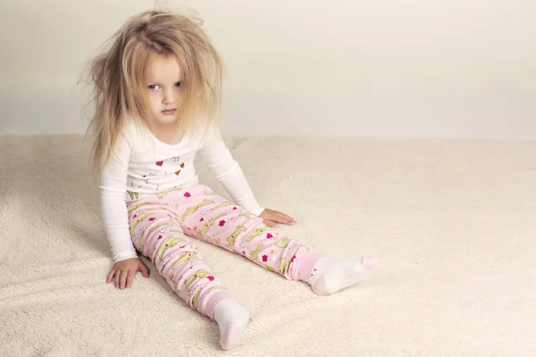 Funny little girl in pyjamas sitting on beige carpet