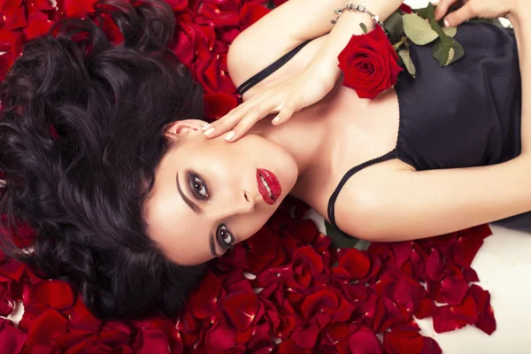 Beautiful woman with dark curly hair lying on carpet from rose\'s petals