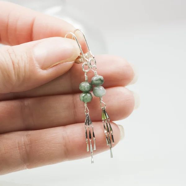 Hand holding silver earrings with emerald gemstones