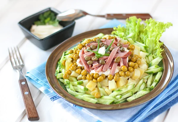 Polish salad with potatoes, ham, cucumber, green peas, capers an