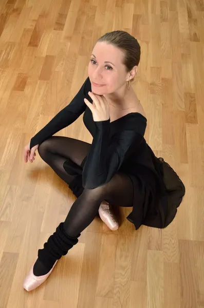 A dancer in black tights and a swimsuit sits on the floor