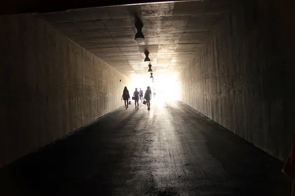 People are walking through dark tunnel