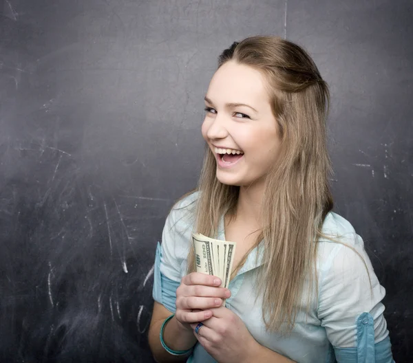 Portrait of happy cute student with money, near blackboard