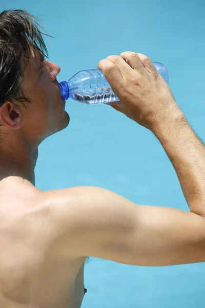 Attractive man drinks water at the swimming pool