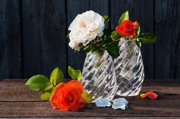 Two glass vases with white and orange roses in the old wooden table