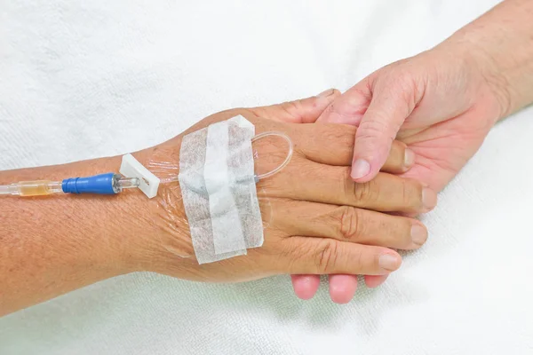 Old hands holding each other with IV solution in a patient\'s hand