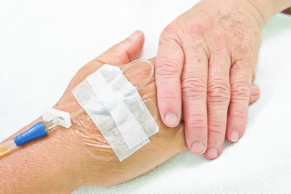 Old hands holding each other with IV solution in a patient\'s hand