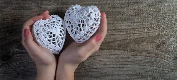 Woman hands holding white lace hearts on old wood background. Valentine\'s day.
