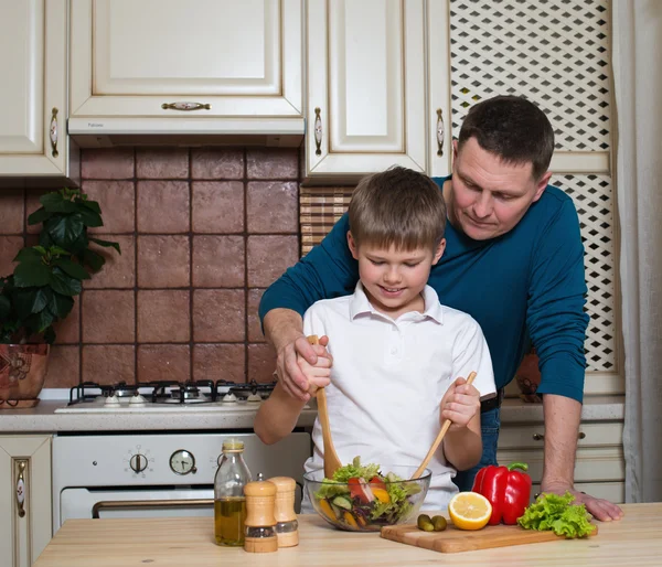 Father and son preparing vegetable salad in the kitchen.
