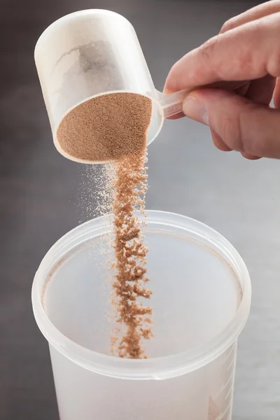 Scoop of chocolate whey isolate protein tossed into plastic white shaker, with focus on the protein in the scoop and falling protein blurred