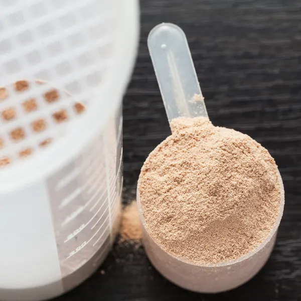 Scoop of chocolate whey isolate protein in front of protein shaker and its parts