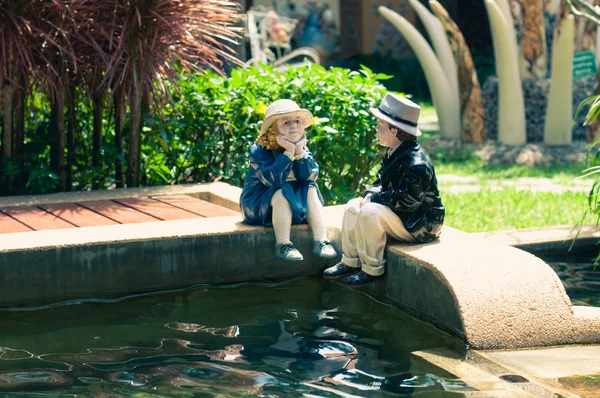 Ceramic woman and man on the edge of a fish pool for garden deco