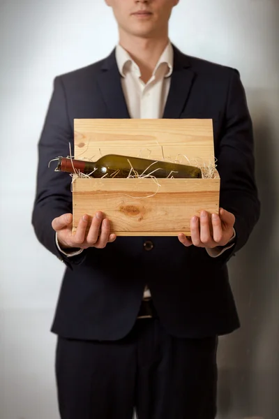 Elegant man in black suit carrying wooden box with wine