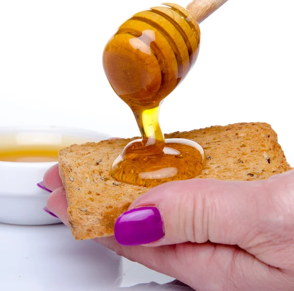 Woman\'s hand holding a toast with honey flowing from a  honey di