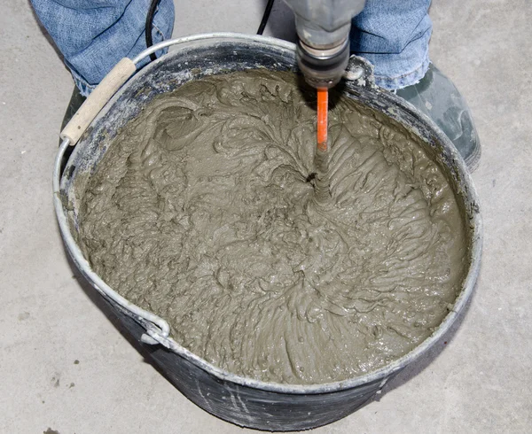 Tiler mixing tile adhesive with power drill in a bucket