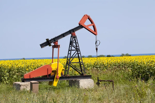 Oil pump with sunflowers field on the background