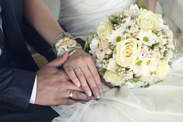 Bride and groom\'s hands with wedding rings and bouquet of flowers