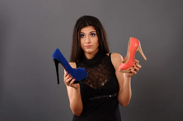 Portrait of a woman trying to decide between two pairs of high heeled shoes