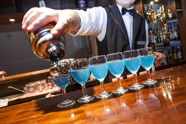 Barman pouring blue coloured drinks to the glasses on the bar co