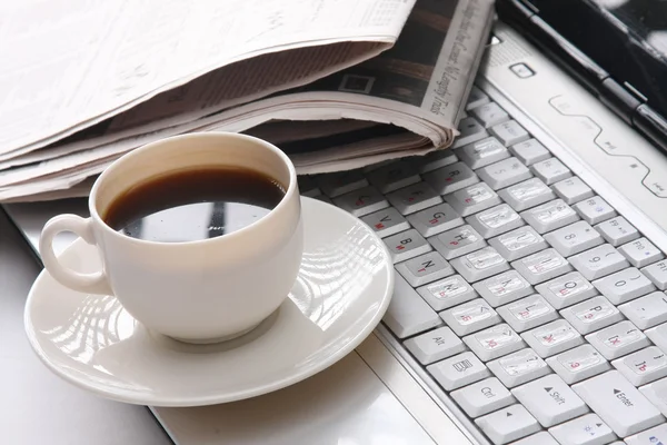 Cup of coffee and a newspaper on a laptop