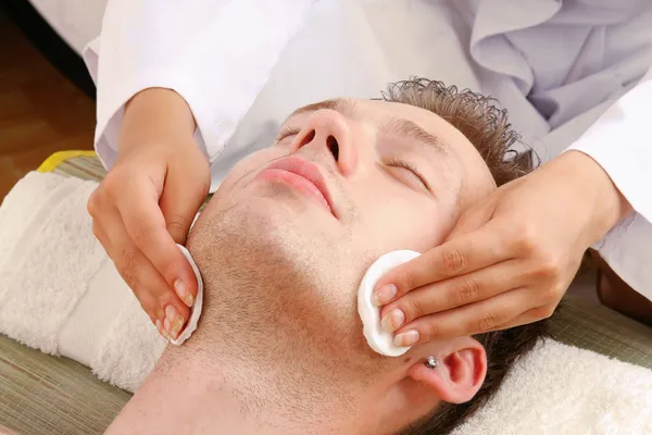 Female hands cleaning man's face with cotton swabs