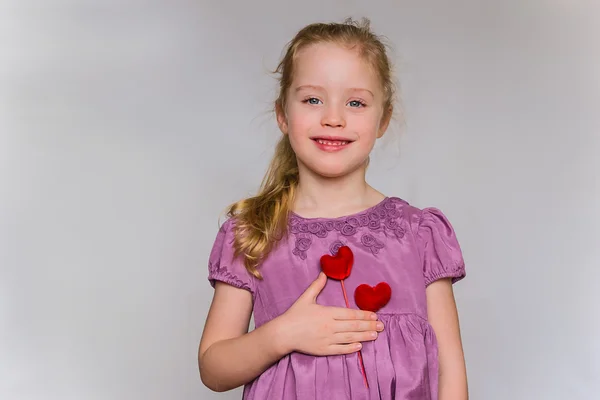 Strawberry blonde preschool girl holds two red heart pattern near her heart