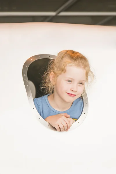Smiling little girl looking out the porthole of a miniature aircraft model