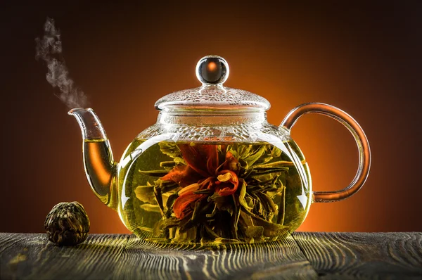 Glass teapot with blooming tea flower on wooden table