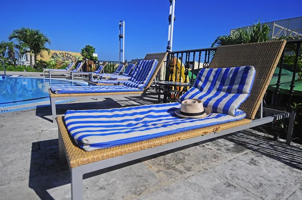 View of striped long deck chairs set by swimming-pool