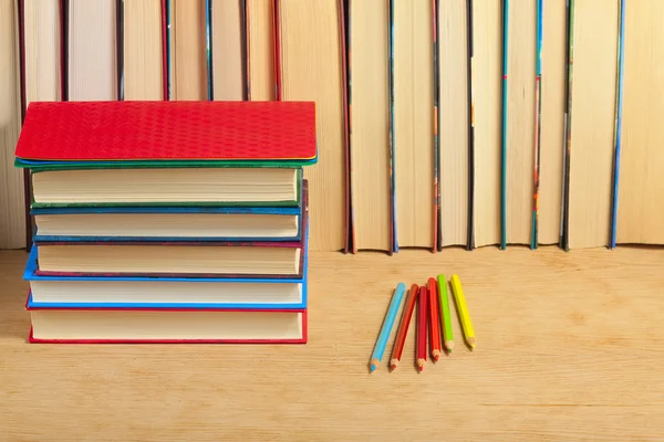 Pile of books and colored pencils on a wooden surface against th