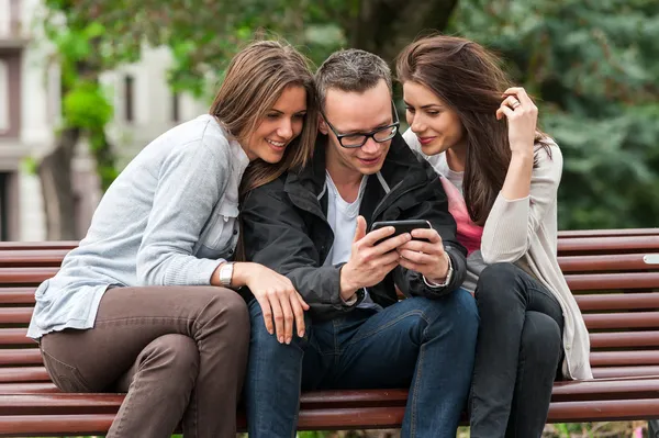 Three friends looking at an image on a smartphone while sitting on a park bench