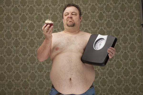 Overweight male holding scales and cupcake